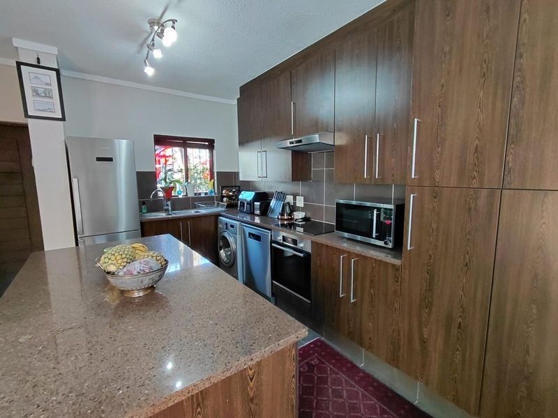 A functional kitchen featuring dark wood cabinetry, stone countertops, a central island, and integrated appliances including an oven, hob, and extractor fan.