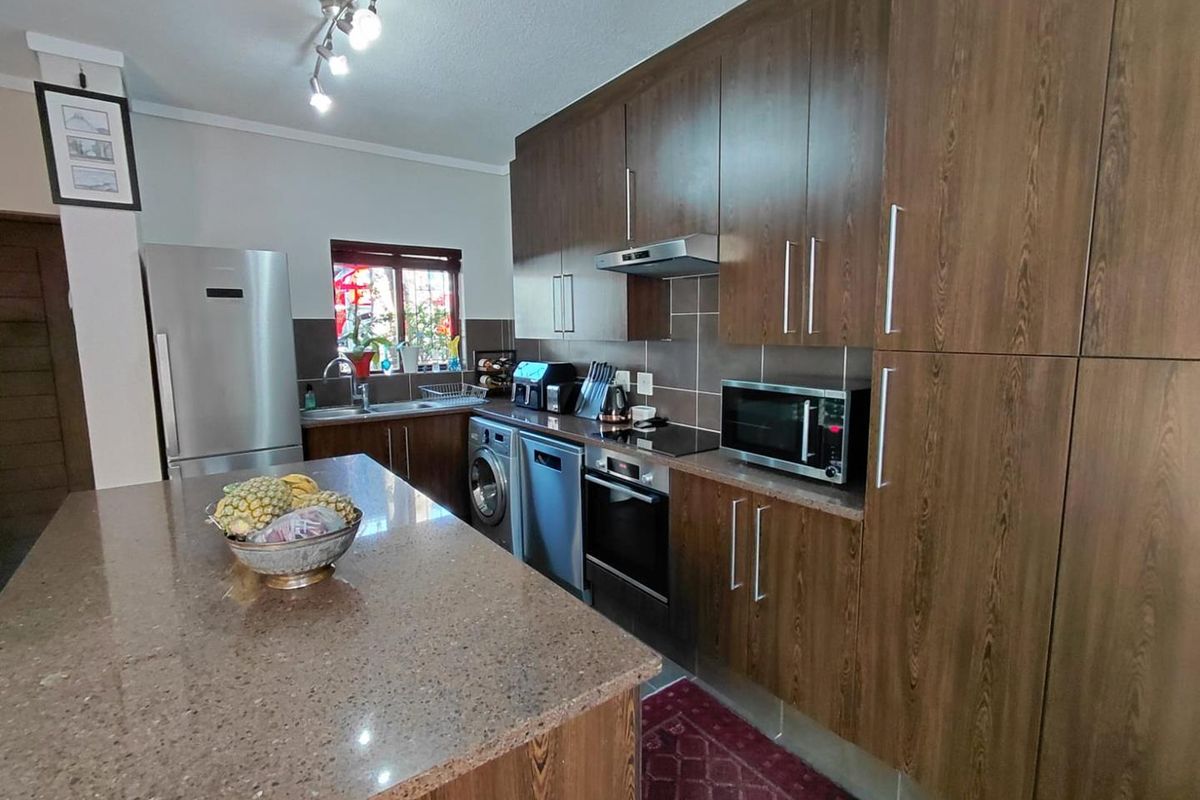 A functional kitchen featuring dark wood cabinetry, stone countertops, a central island, and integrated appliances including an oven, hob, and extractor fan.