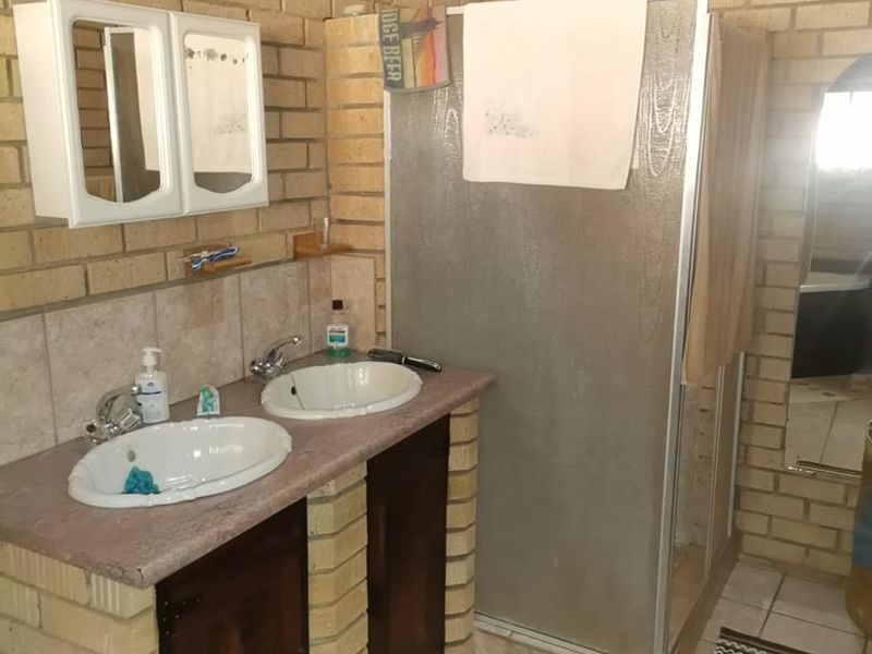 Bathroom featuring a double vanity with drop-in sinks, a shower enclosure, and exposed brick walls with tiled flooring.