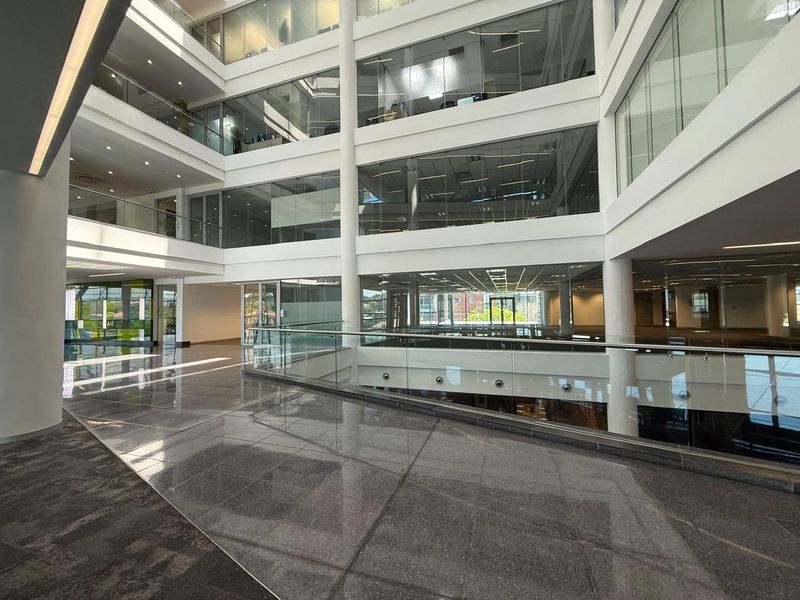 Modern multi-level office atrium featuring polished granite floors, extensive glass partitioning, and a contemporary open-plan architectural design.