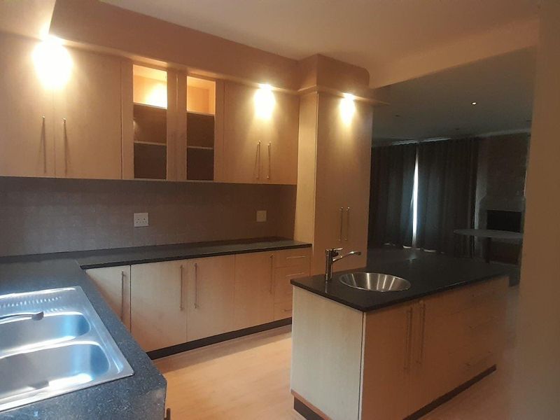 A functional kitchen featuring light wood cabinetry, dark stone countertops, a central island with a prep bowl, and recessed lighting.