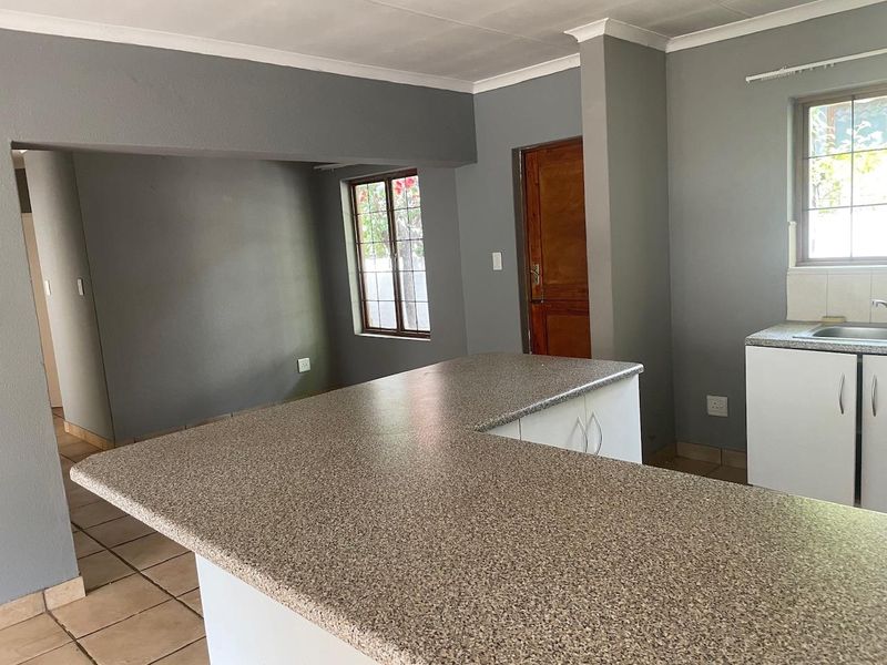 An open-plan kitchen area featuring a central island with laminate countertops, tiled flooring, and neutral grey walls in a vacant space.