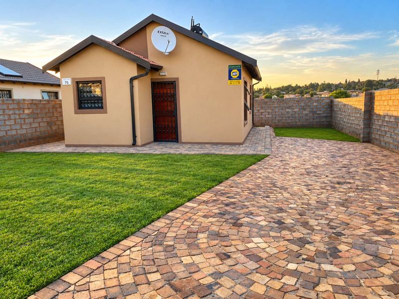 A well-maintained single-story house featuring a paved driveway, manicured lawn, and secure boundary walls, presenting a neat and tidy street-facing facade.