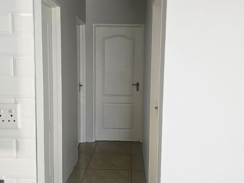 A clean, neutral hallway featuring tiled flooring, white internal doors, and classic cove cornice detailing.