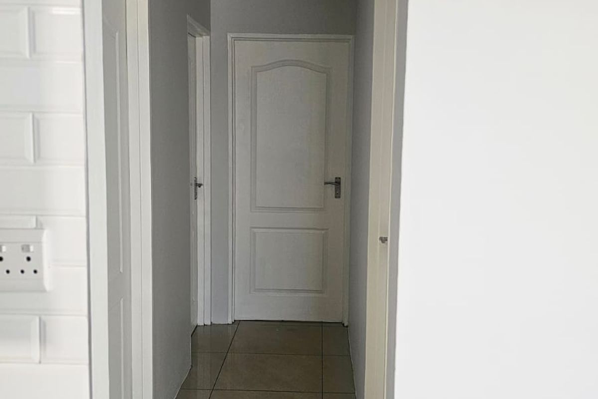 A clean, neutral hallway featuring tiled flooring, white internal doors, and classic cove cornice detailing.