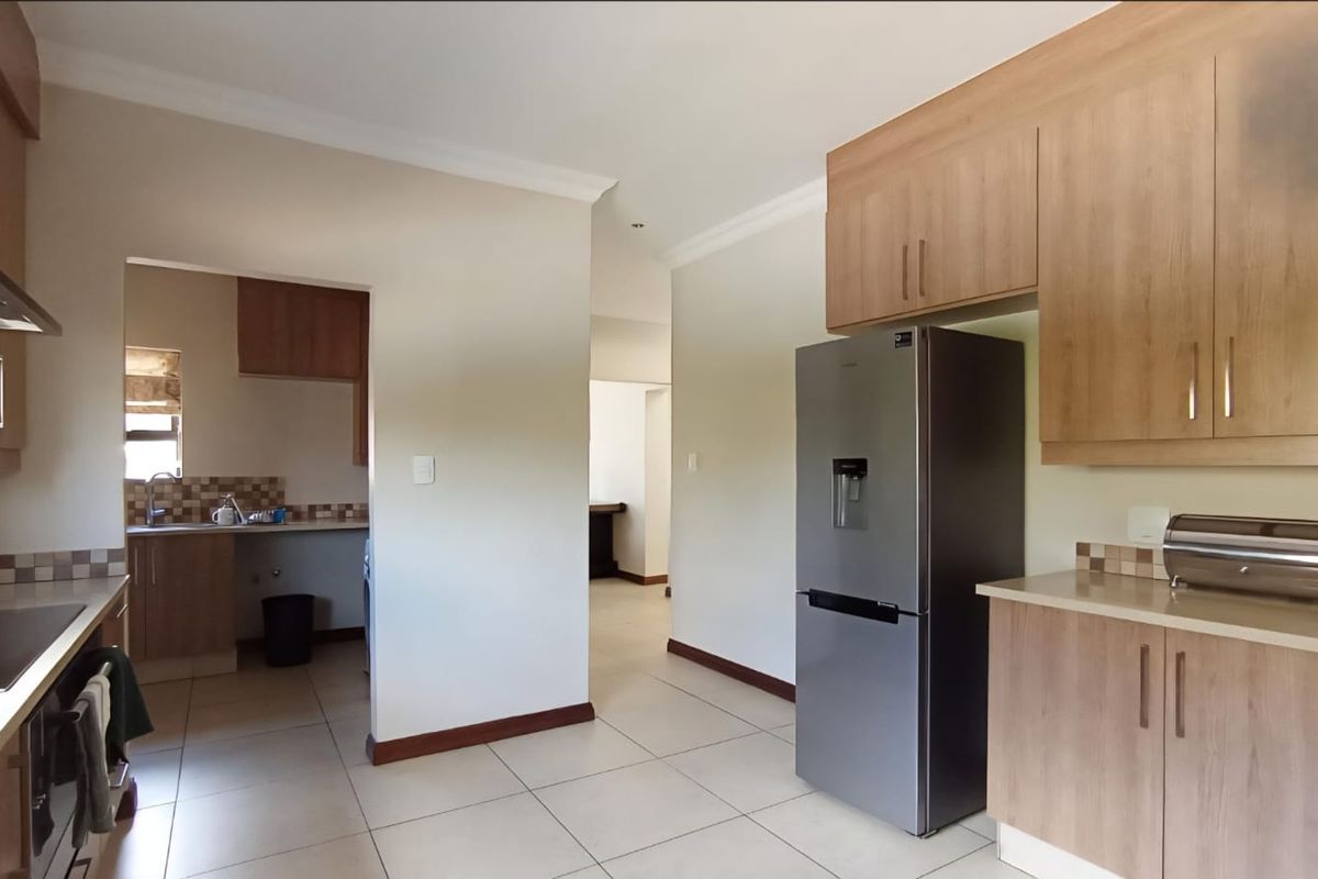 A functional kitchen featuring light wood cabinetry, stone-look countertops, a built-in hob, extractor fan, and an adjacent scullery area with additional sink and storage.