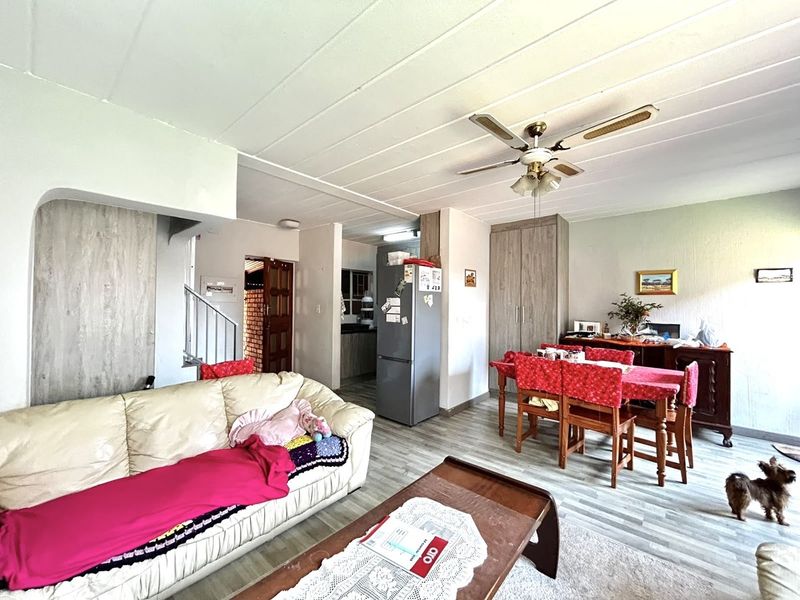 Open-plan living and dining area featuring laminate flooring, a ceiling fan, and built-in storage, with an adjacent kitchen visible in the background.