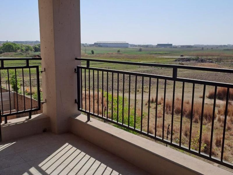 A spacious covered balcony featuring tiled flooring and a metal balustrade, offering expansive views of the surrounding landscape.