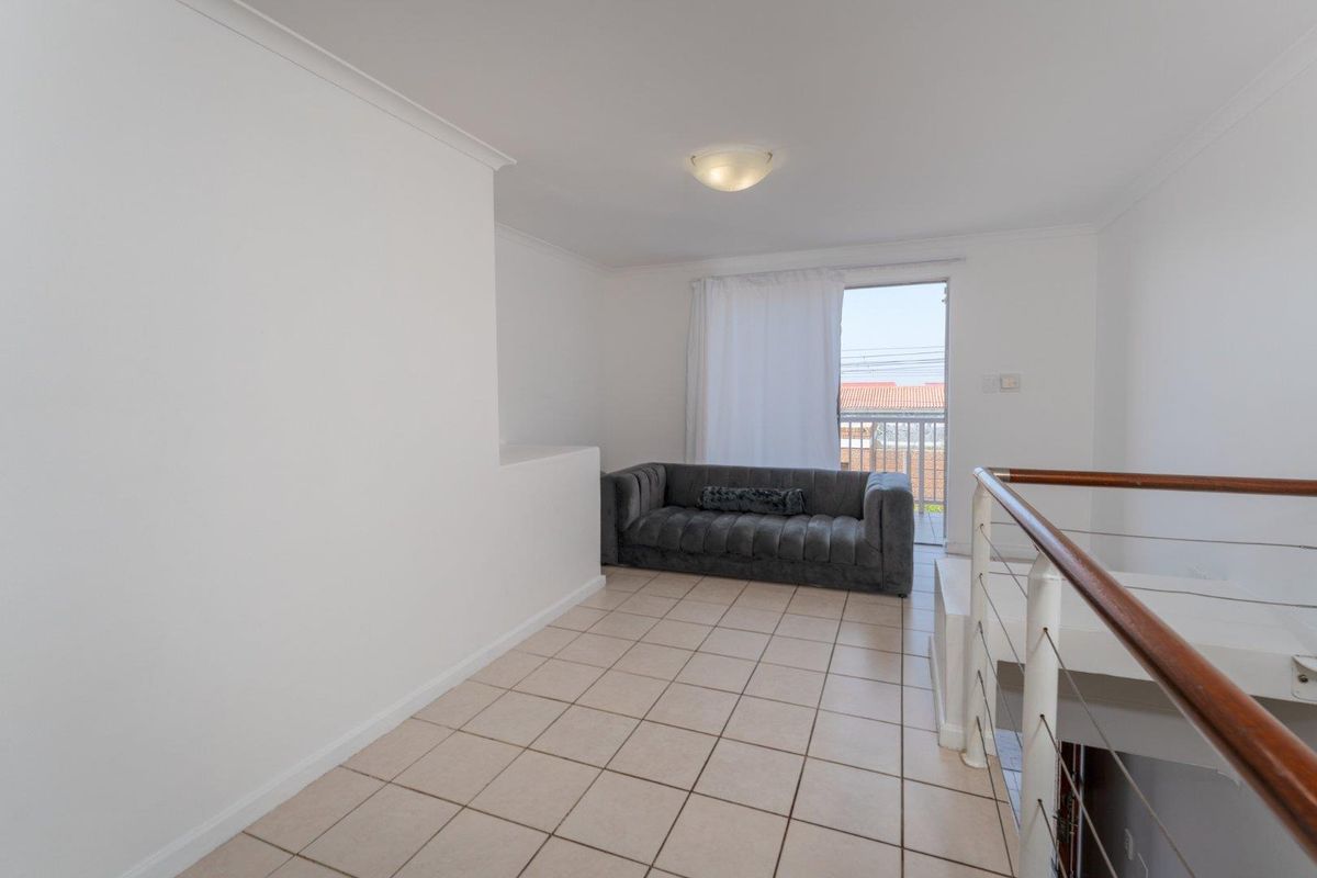 A bright living area featuring tiled flooring, a staircase with a wooden handrail, and a sliding door providing access to a balcony.