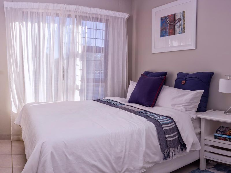 A well-lit bedroom featuring neutral wall tones, tiled flooring, and a large window with sheer curtains.