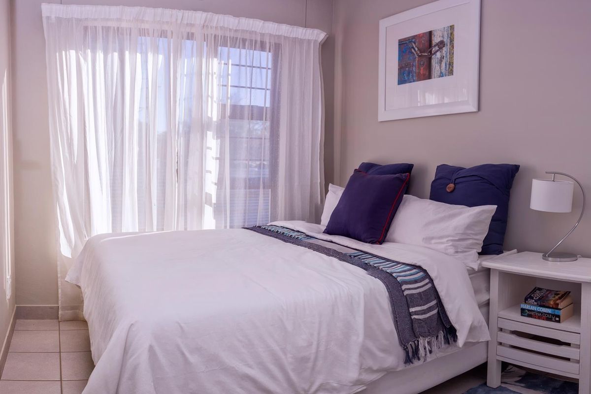 A well-lit bedroom featuring neutral wall tones, tiled flooring, and a large window with sheer curtains.