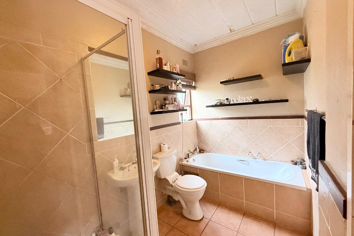 A functional bathroom featuring a tiled bathtub, separate glass-enclosed shower, pedestal basin, and toilet with neutral wall and floor tiling.
