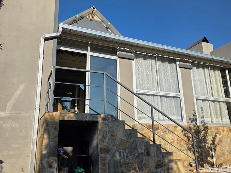 Rear exterior view of the house featuring stone cladding, a metal staircase with railing, and sliding glass door access to the upper level.