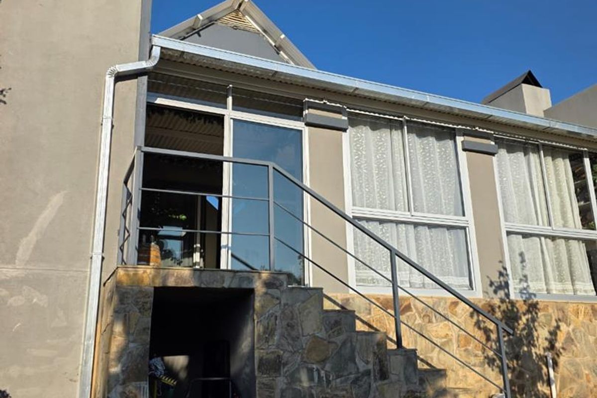 Rear exterior view of the house featuring stone cladding, a metal staircase with railing, and sliding glass door access to the upper level.