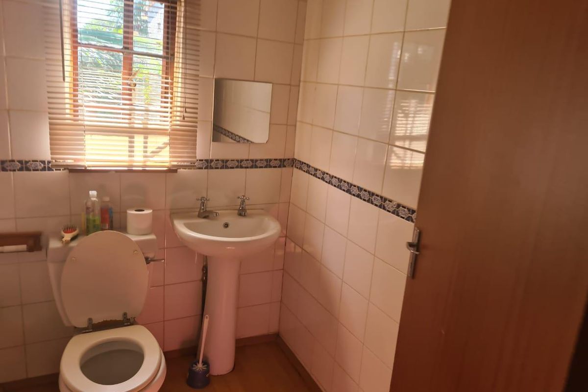 A functional bathroom featuring a pedestal basin, toilet, and tiled walls with a decorative border.