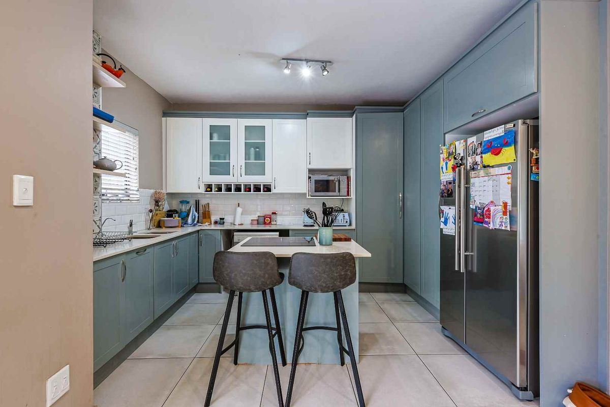 Modern kitchen featuring two-tone cabinetry, a central island with integrated cooktop, tiled flooring, and subway tile backsplash.