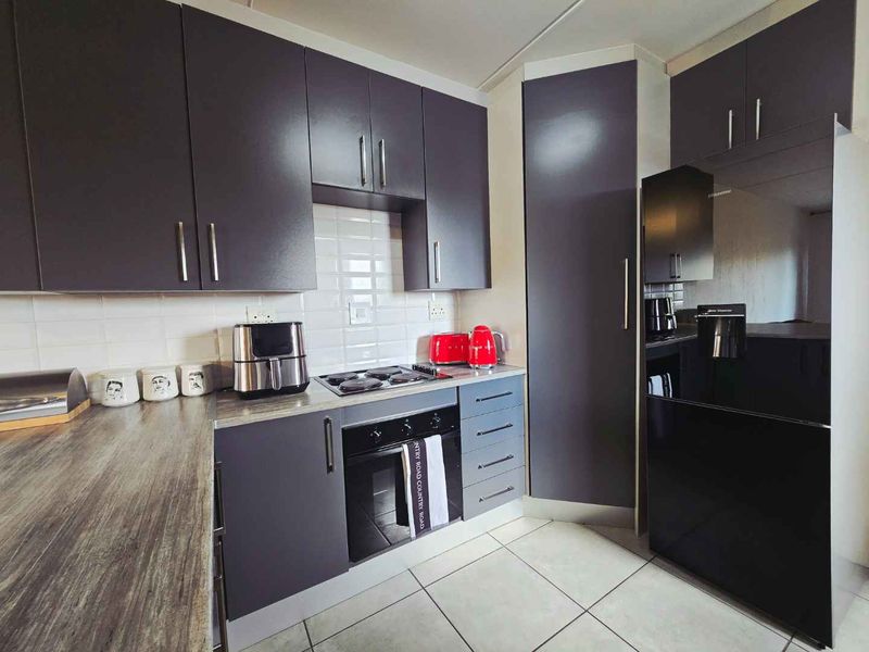 Modern kitchen featuring dark grey cabinetry, wood-look laminate countertops, subway tile backsplash, and integrated electric oven and hob.