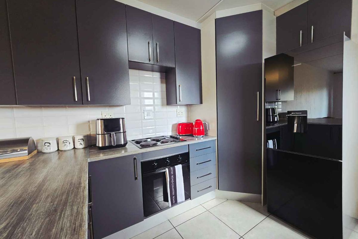 Modern kitchen featuring dark grey cabinetry, wood-look laminate countertops, subway tile backsplash, and integrated electric oven and hob.