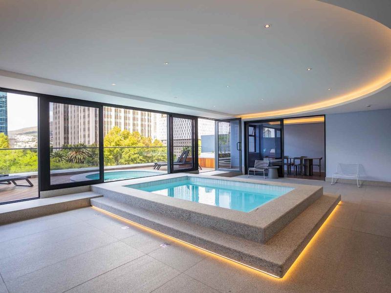A luxurious indoor pool area featuring a raised tiled pool, recessed ceiling lighting, and large sliding glass doors opening to an outdoor terrace.