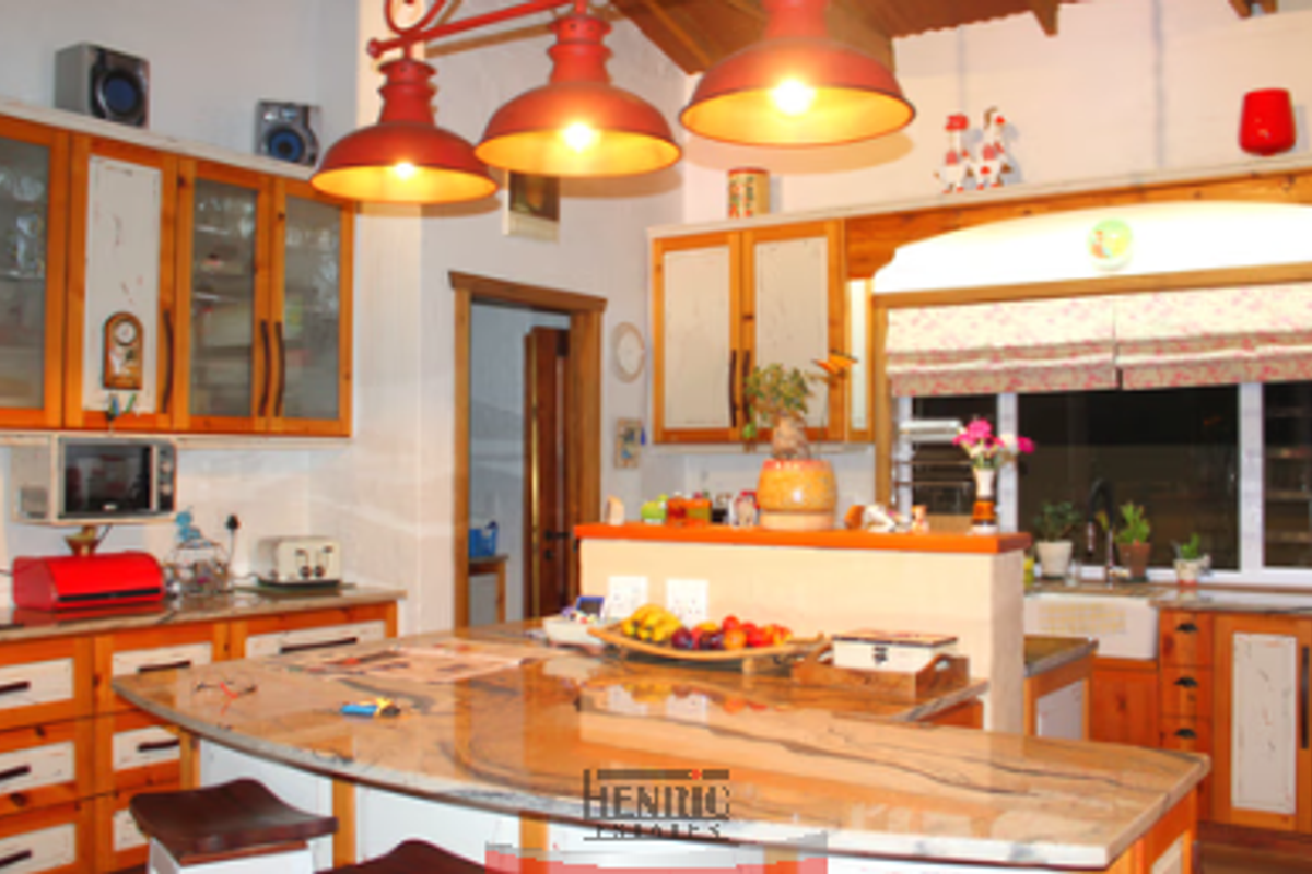 A rustic-style kitchen featuring wooden cabinetry, a large stone-topped island, and distinctive red pendant lighting over the workspace.
