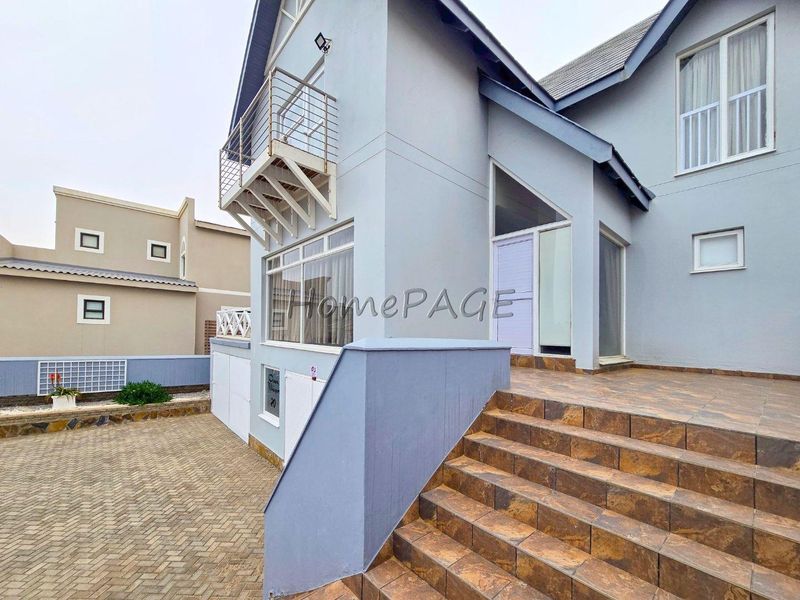 Front exterior view of a multi-level house featuring a tiled staircase, paved driveway, and a balcony with metal railing.