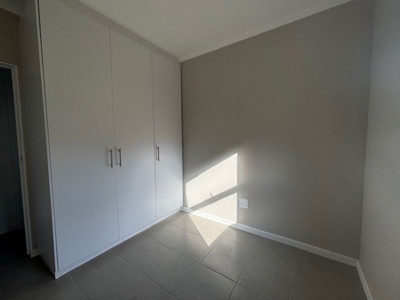 A clean, empty bedroom featuring neutral wall tones, tiled flooring, and ample built-in cupboard storage.