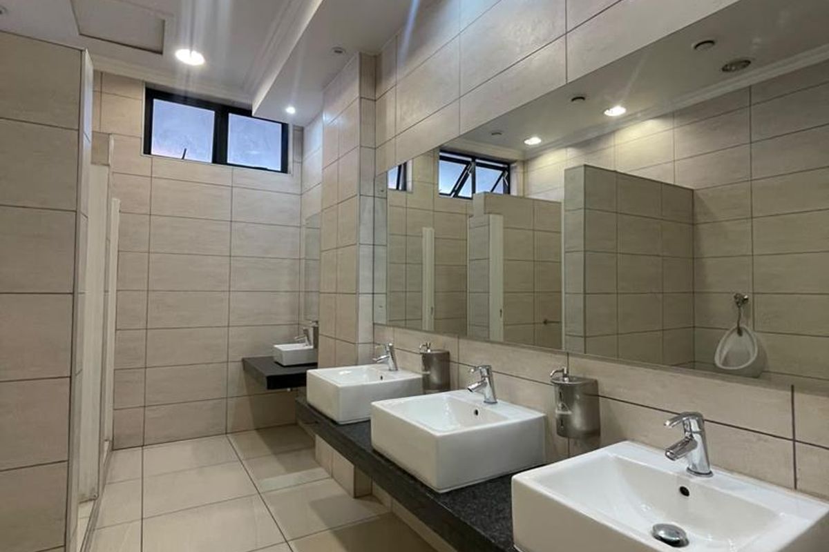 Modern commercial bathroom featuring a long granite vanity with multiple vessel sinks, large wall-mounted mirrors, and neutral ceramic tiling throughout.