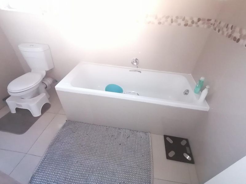 A functional bathroom featuring a built-in bathtub and a standard toilet with neutral wall finishes and tiled flooring.