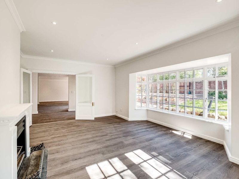 Bright and spacious living room featuring a classic fireplace, large bay window, and elegant crown molding with neutral finishes throughout.