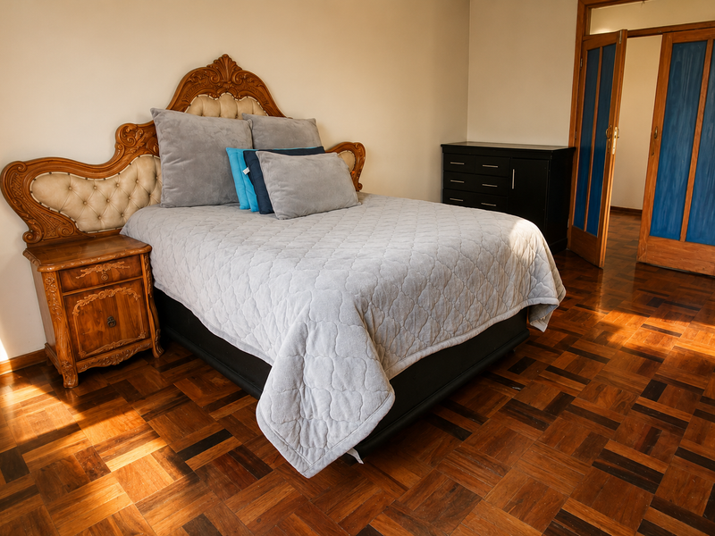 A bedroom featuring polished parquet flooring and a wooden double door entrance, providing a warm and classic aesthetic.