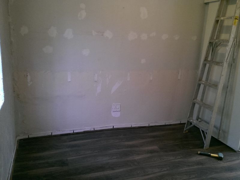 An office space currently undergoing renovations, featuring new dark laminate flooring and walls prepared for finishing.