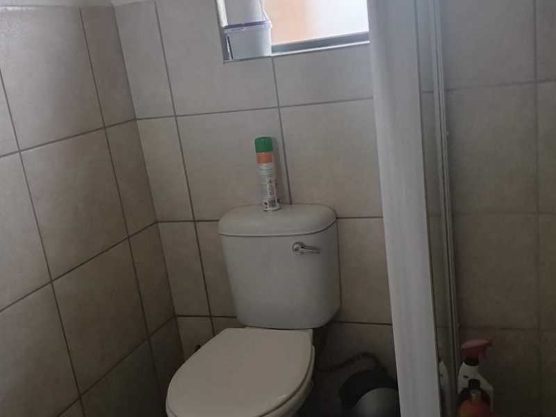 A functional bathroom featuring tiled walls and flooring, equipped with a standard toilet and a window for natural light.