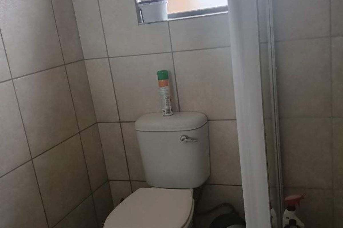 A functional bathroom featuring tiled walls and flooring, equipped with a standard toilet and a window for natural light.