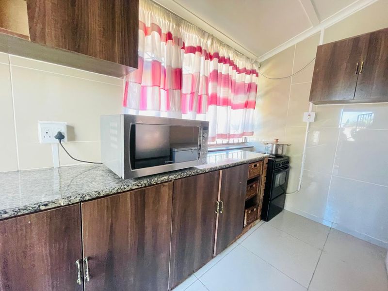 A functional kitchen featuring dark wood cabinetry, granite countertops, tiled backsplash, and tiled flooring, providing a practical workspace for daily cooking.