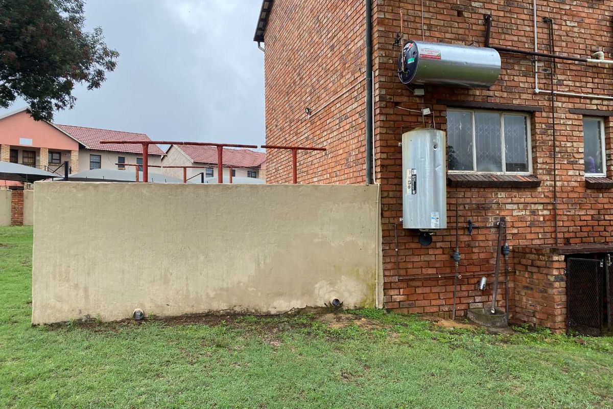 Exterior view of the apartment building featuring exposed brickwork, external water heating units, and a concrete boundary wall.