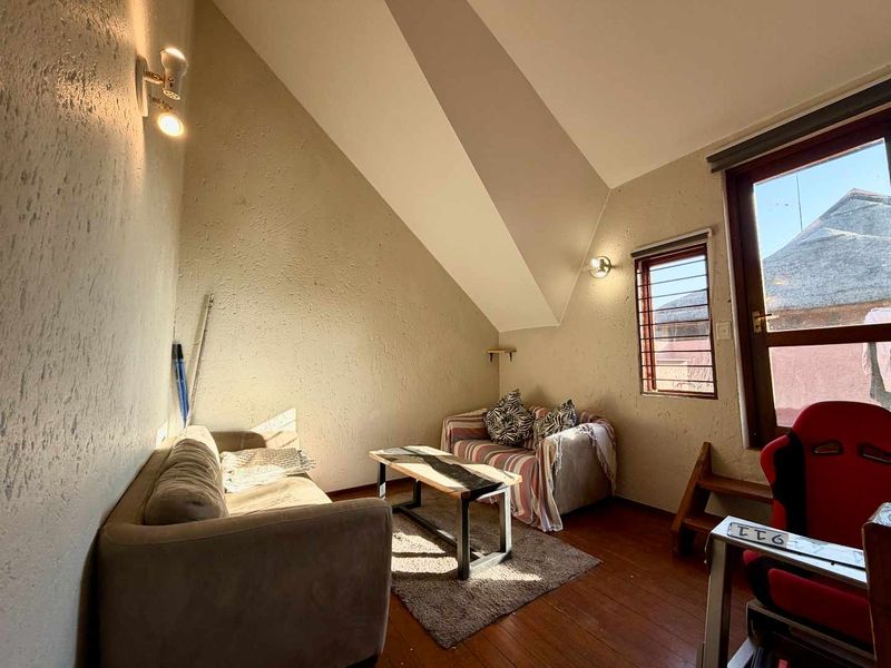 A cozy living area featuring a unique sloped ceiling, timber flooring, and natural light from a window with security bars.