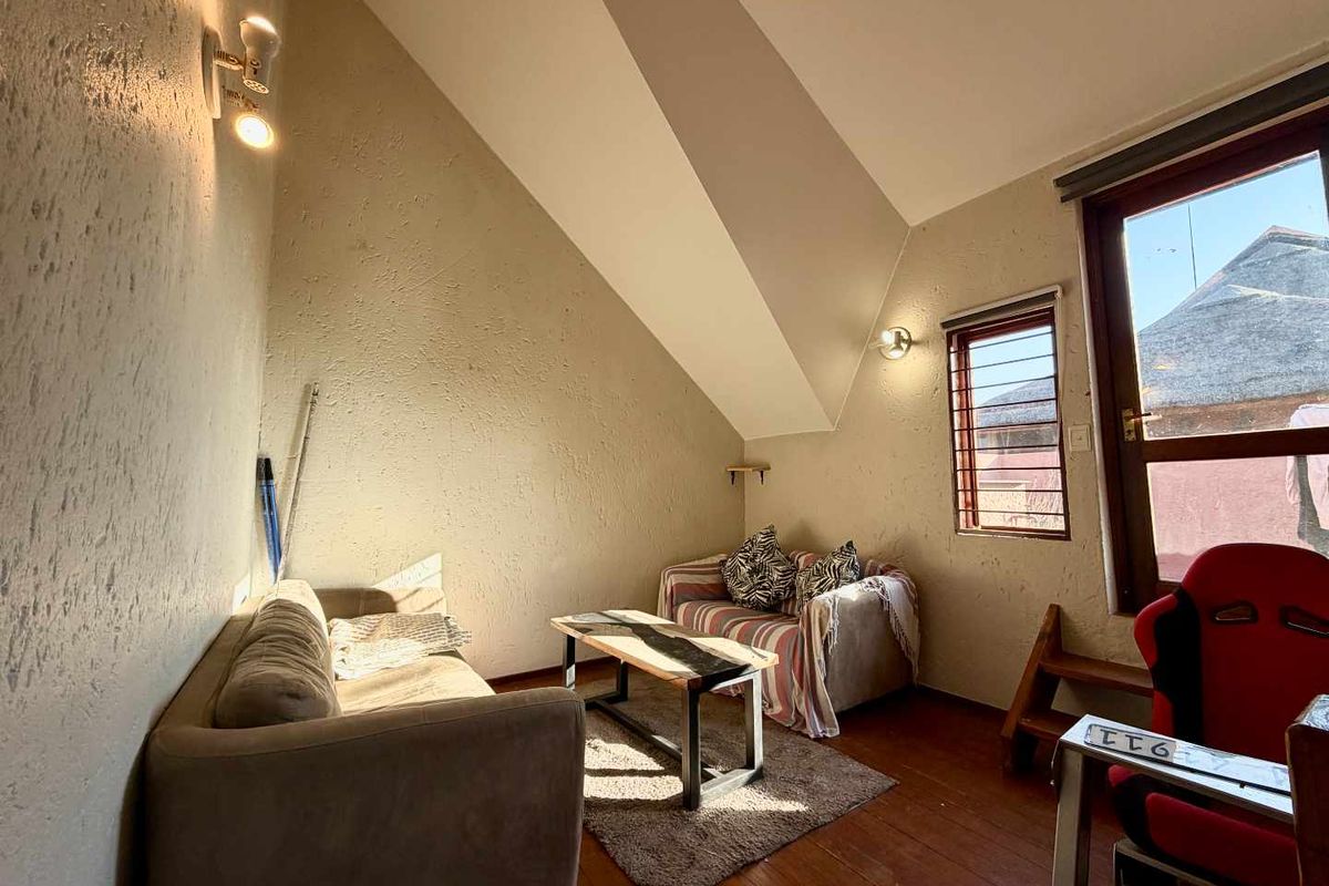 A cozy living area featuring a unique sloped ceiling, timber flooring, and natural light from a window with security bars.