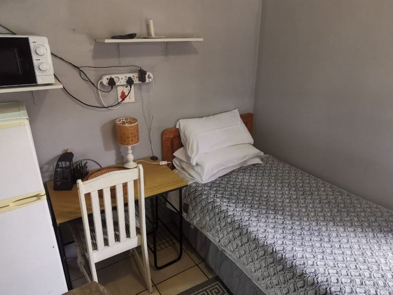 A compact bedroom featuring tiled flooring and wall-mounted shelving, currently utilized as a multi-functional living space.