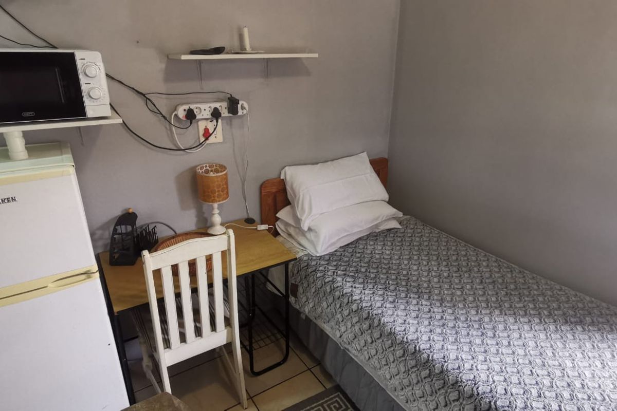 A compact bedroom featuring tiled flooring and wall-mounted shelving, currently utilized as a multi-functional living space.