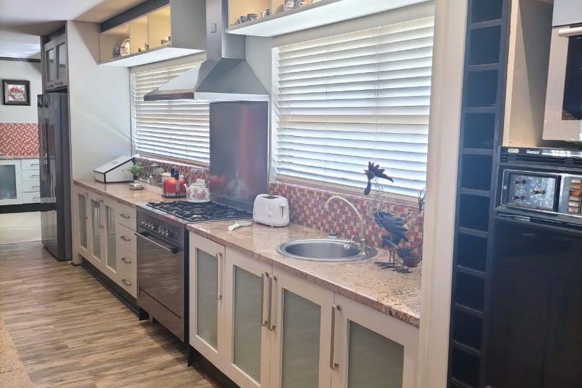 A well-appointed kitchen featuring granite countertops, integrated cabinetry, a stainless steel extractor fan, and a built-in oven, finished with modern wood-look flooring.
