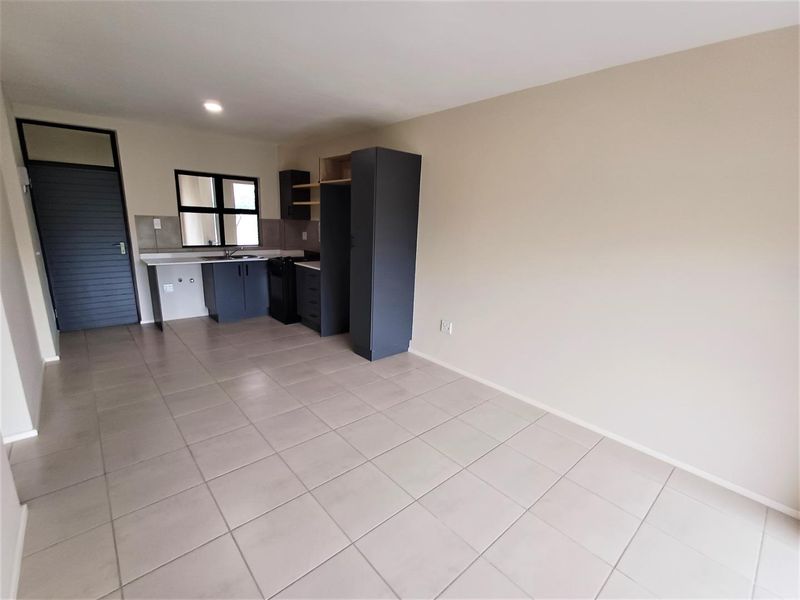 An open-plan living and kitchen area featuring modern dark cabinetry, tiled flooring, and neutral wall finishes in a clean, vacant space.
