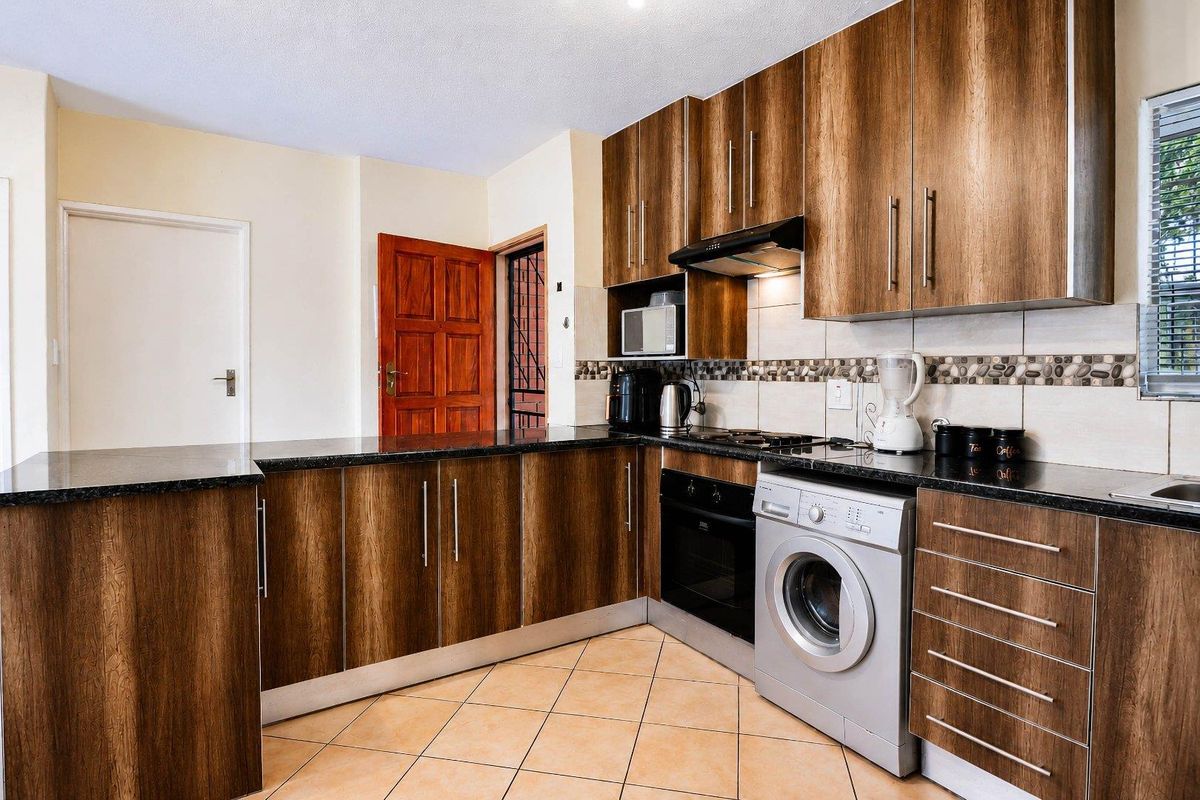 A functional kitchen featuring wood-grain cabinetry, dark granite countertops, a built-in oven, extractor fan, and tiled flooring.