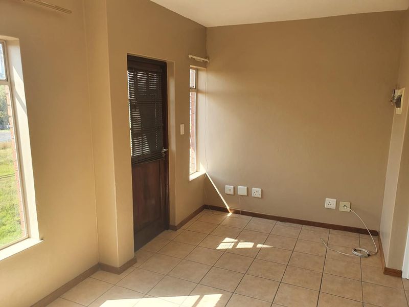 An empty living area featuring tiled flooring, neutral wall tones, and direct access to an outdoor space via a timber door.