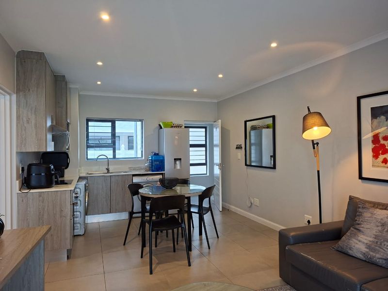Modern open-plan living area featuring a compact kitchen with built-in cabinetry, tiled flooring, and recessed lighting, seamlessly integrated with the dining and lounge space.