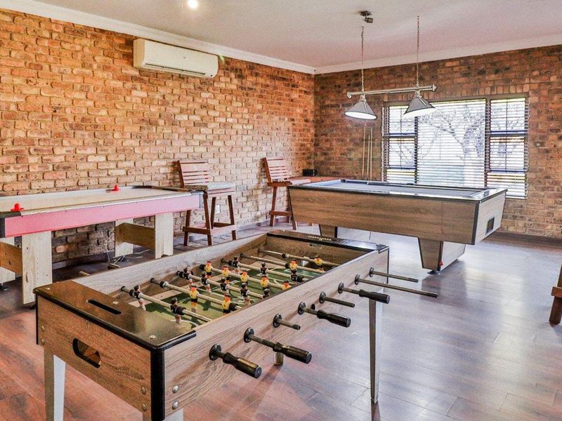 A spacious games room featuring exposed brick walls, laminate flooring, and integrated air conditioning, currently set up as an entertainment area.
