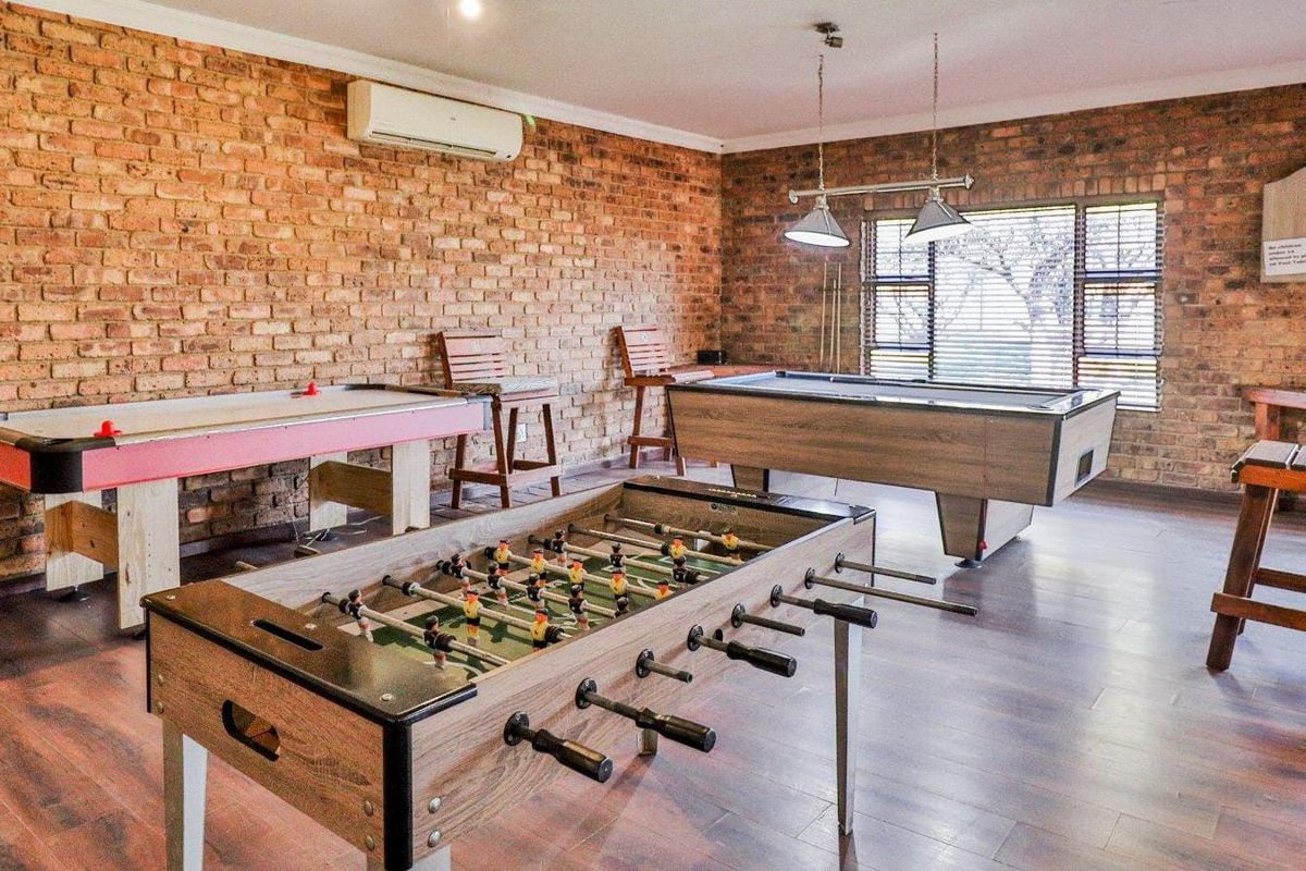 A spacious games room featuring exposed brick walls, laminate flooring, and integrated air conditioning, currently set up as an entertainment area.