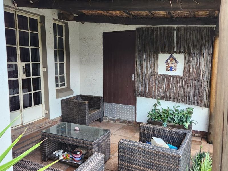 A covered patio area featuring a rustic thatched roof with exposed timber beams and tiled flooring, providing a sheltered outdoor living space.