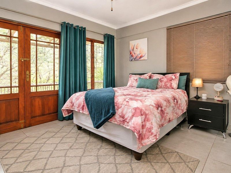 A well-maintained bedroom featuring tiled flooring, neutral wall tones, and direct access to an outdoor balcony through a wooden framed glass door.