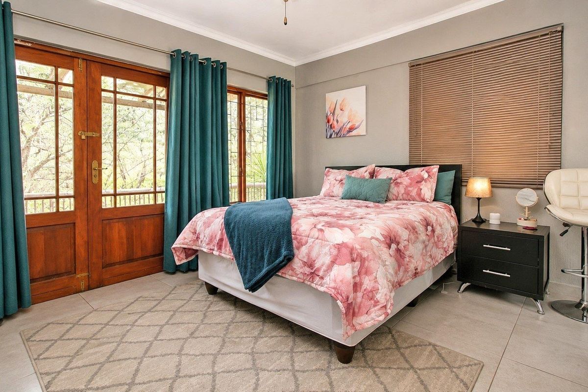 A well-maintained bedroom featuring tiled flooring, neutral wall tones, and direct access to an outdoor balcony through a wooden framed glass door.