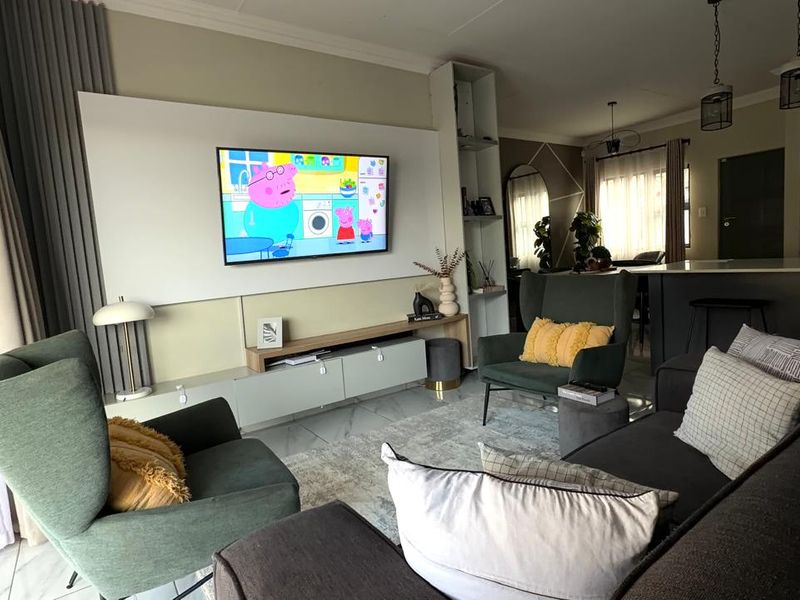 Modern open-plan living area featuring a sleek built-in media wall, kitchen island with breakfast bar, and large sliding doors leading to outdoor space.